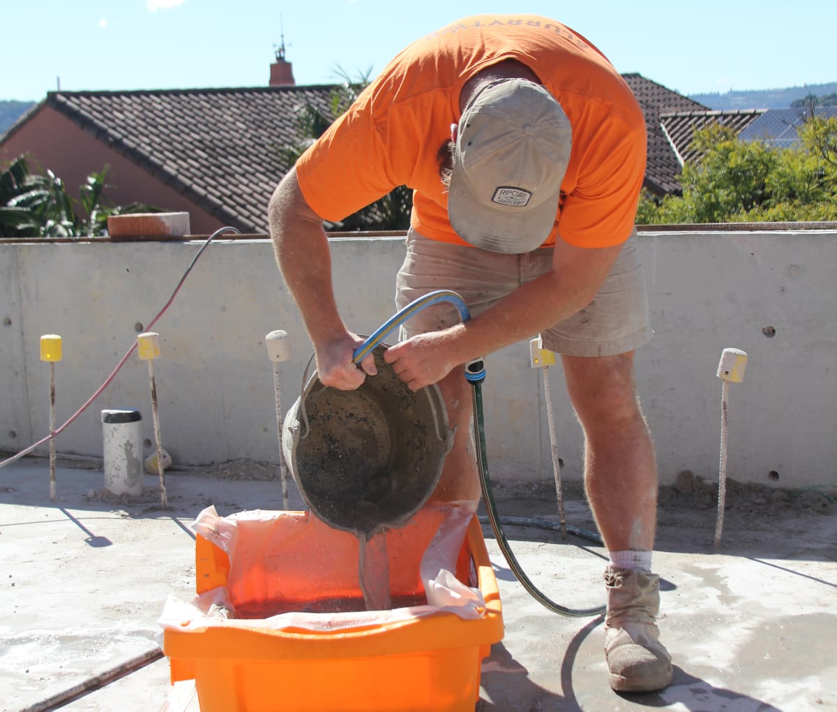 Man in orange shirt and hat rinsing a bucket into a slurrytub.